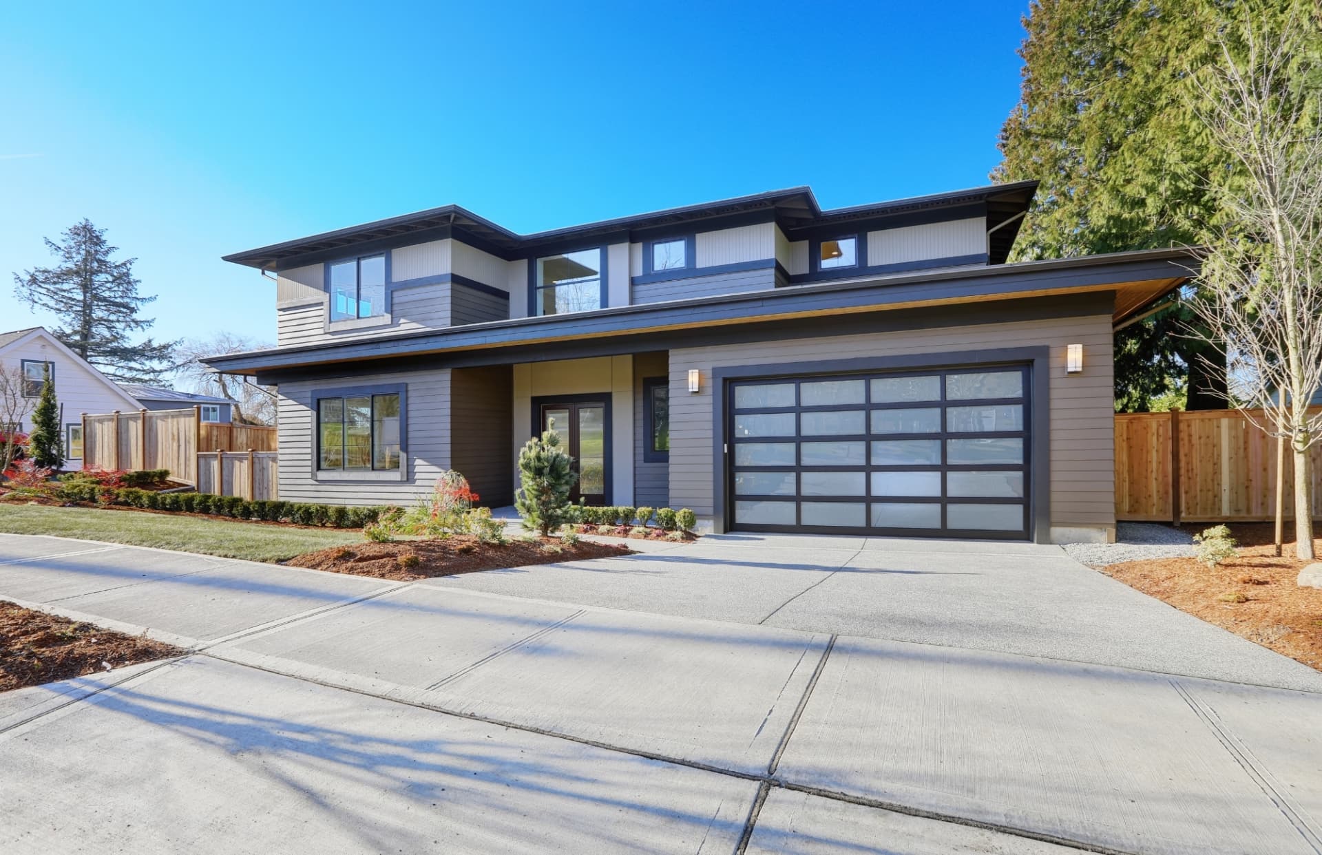 A modern two-storey house seen from the driveway, with wide low-slope roof overhangs above the garage and entry.